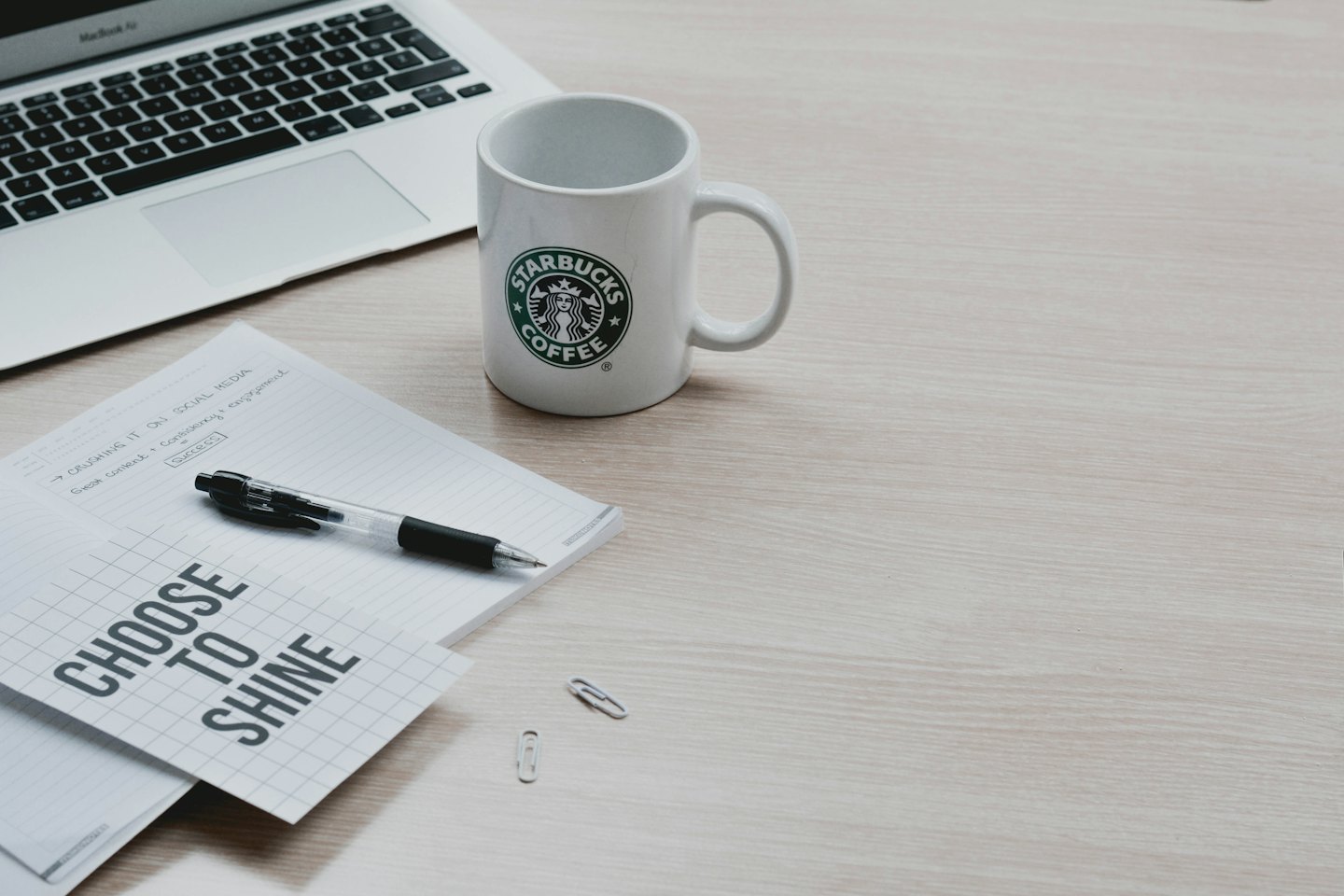 Ein Laptop, Notizbuch und Kaffeetasse auf einem Schreibtisch.